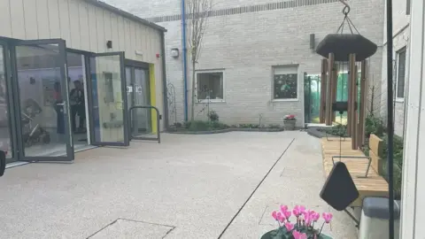 BBC An image of the secret garden, showing walkways, benches, planted flowerbeds and a wind chime