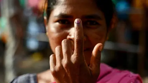 AFP via Getty Images A woman shows her inked finger after casting her ballot to vote at a polling station as voting starts during the first phase of India's general election in India in June 2024.