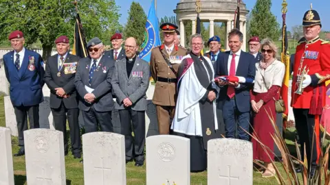 Family and military party stand at the headstone of LCpl Voice MM.