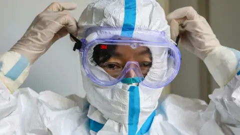 Getty Images This photo taken on January 30, 2020 shows a doctor putting on a pair of protective glasses before entering the isolation ward at a hospital in Wuhan in China's central Hubei province