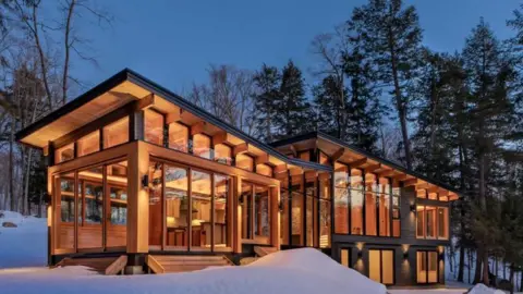 Adrian Ozimek/Trevor McIvor Architect Inc A cottage in the snow. The lights are on and there are trees around it.