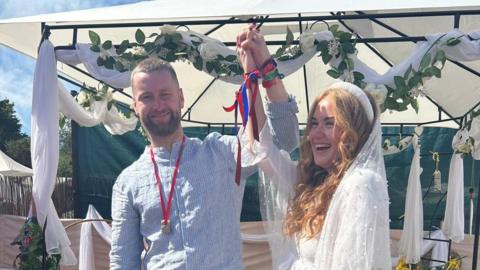 Alex Bee and Liam Barnett lift their arms in the after getting married at Glatstonbury
