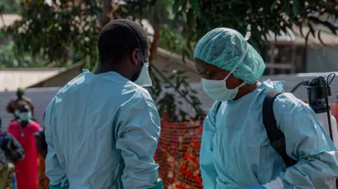 Two health workers are pictured wearing blue protective gear