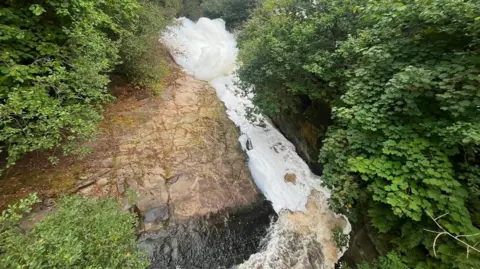 Craig Hannah Large white clumps of foam in a river.