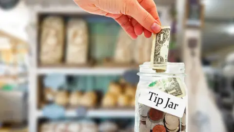iStock/Getty Images Stock photo of someone putting money into a tip jar