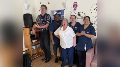 Essex Partnership University NHS Foundation Trust  Marcus Brown performing with a guitar at Clifton Lodge, with staff joining in to sing for residents and their families