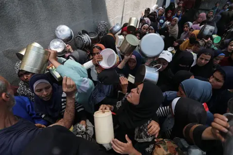 Getty Images Palestinians, including children, wait in line to receive hot meals distributed by the charity organisations at Nuseirat Refugee Camp in Deir al-Balah, Gaza on June 4, 2025