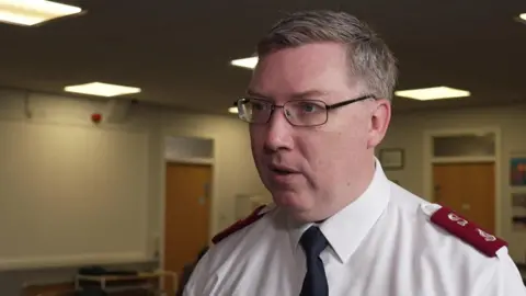 The Salvation Army's Major Richard Thompson is wearing a white shirt with maroon epaulettes and a black tie.