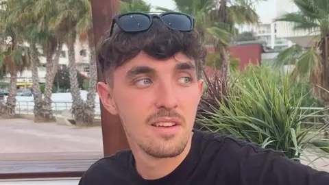 Sam Knight, looking away from the camera. He has dark hair and sunglasses on his head.