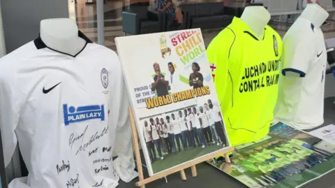Julita Waleskiewicz Three football shirts displayed on mannequins alongside a board featuring Team India's victory at the 2010 Street Child World Cup. The display forms part of the Striving for Unity exhibition.
