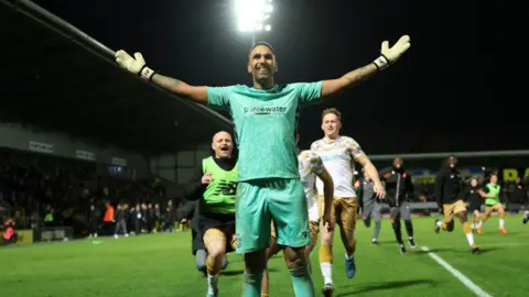 Getty Images Goalkeeper Jasbir Sing in a green strip with his arms outstretched as team-mates run to celebrate with him