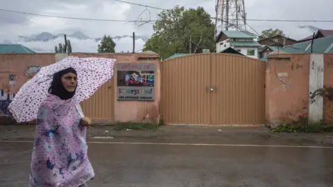 Abid Bhat A woman walks in front of a shut primary school