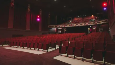 Hebden Bridge Picture House A cinema auditorium, featuring rows of red seats in the lower stalls level, as well as a dress circle above. The carpet and the walls are also red.