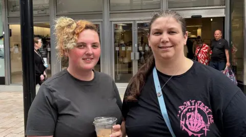 Two women looking into the camera smiling, in front of the M&S store