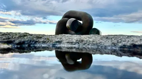 BBC Two giant chain links on a rock reflected in a puddle