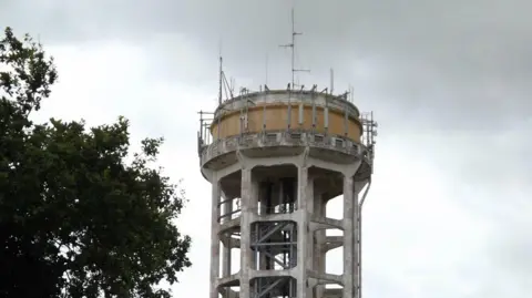 A close-up of the top of the Trimley St Mary water tower - a large concrete and steel tower with telecommunication equipment on top. 