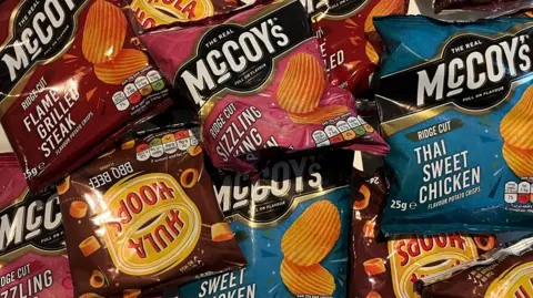 Packets of McCoy's and Hula Hoops crisps sit on a table. 