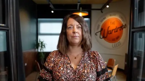 A woman with short brown hair is wearing a flower print blouse. She's staring directly at the camera with a serious expression