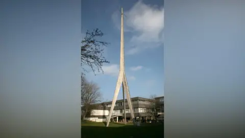 City of Durham Parish Council Concrete three pronged tower (at its base) standing high above a grey building on a sunny day. 