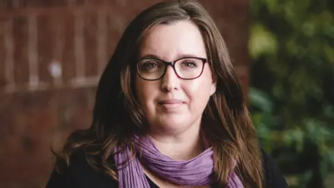 Dr Siobhan O'Dwyer A woman with glasses and a purple scarf looking at the camera