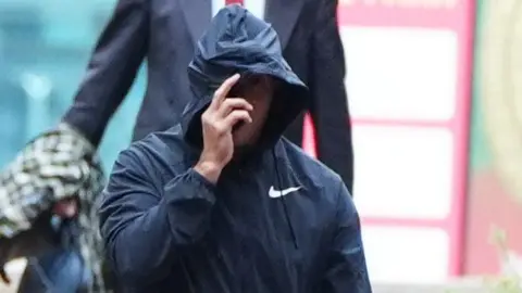 PA Media Curtis Warren, 61, arrives at Liverpool Crown Court, hiding his face under the hood of his windbreaker, and has hand. 