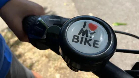 Jon Wright/BBC A close up of a bicycle bell which has I heart by bike written on it.