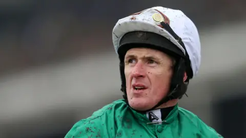 A jockey in his silks with a splatter of mud across his face following a race