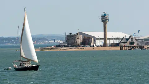 Sailing boat passing Calshot Activities center on the shores of the Solent, Calshot Spit, Southampton, England UK