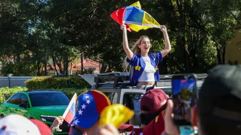 A woman waving a Venezuelan flag with her upper body sticking out on a car.