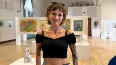 Keele University A woman standing in an art gallery, with paintings and sculptures visible in the background.