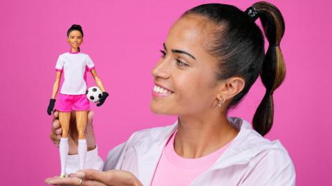 Footballer Mary Fowler holding her Barbie against a pink background