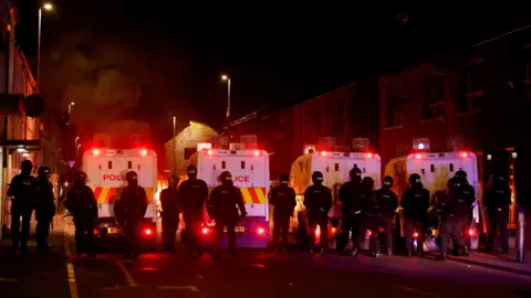 Reuters Serangkaian petugas polisi di malam hari berdiri di depan empat van polisi.