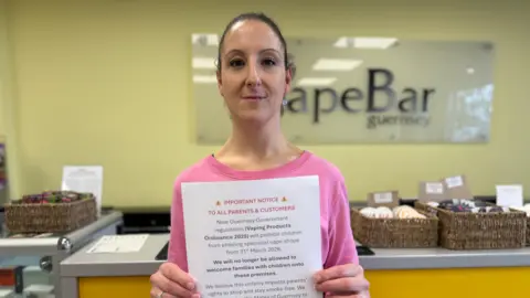 A woman holding a sheet of paper detailing where people can sign the petition. The woman has long brown hair which has been tied back, and is wearing a pink top.