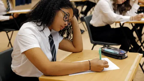 School pupils in white shirts and black ties are taking notes in an exam hall.