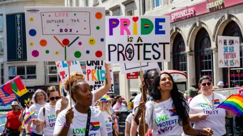 Getty Images A crowd of people at a Pride event. They are all wearing Pride t-shirts and holding up banners and placards. 