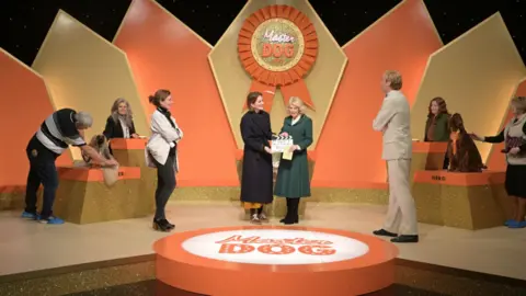 PA Queen Camilla (centre right) holds a clapper board during a visit to the set of the series Rivals in Bristol, to celebrate British television production, youth opportunity in the creative industries, and the legacy of her friend, the author Dame Jilly Cooper. 