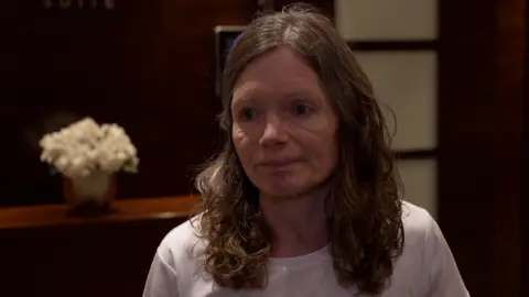 A woman in a dimly lit room wearing a white shirt.
