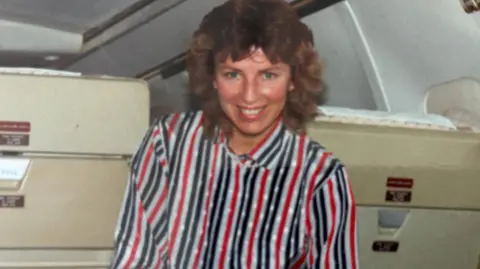 Claire O'Donnell An archive image of Claire O'Donnell from her days as a flight attendant, inside a plane. She is wearing a striped top. She is smiling.