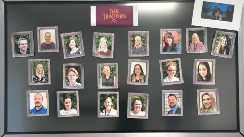 Jo Dyer A black board with 21 photos of teachers stuck on.