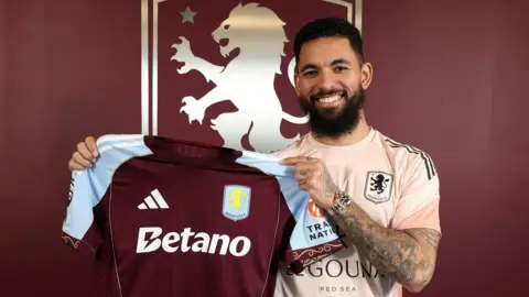 Douglas Luiz smiles as he holds up the Aston Villa shirt at his signing