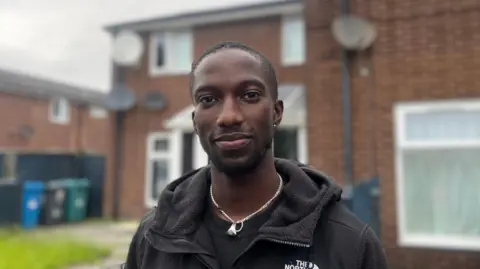 Baka Bah smiling in front of his home in Moss Side