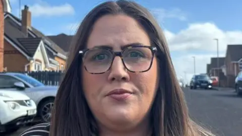 Julie Middleton looking straight down the camera. She is wearing glasses and has long dark brown hair. She's wearing a striped top.