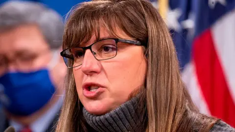 Kara Weipz in a polo neck, wearing glasses; she has long brown hair