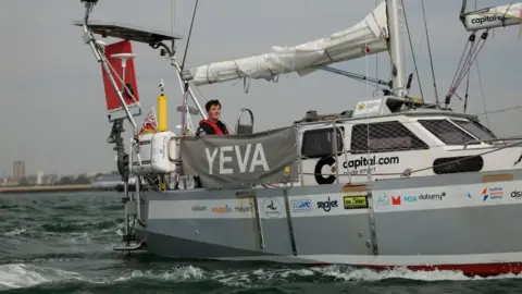 PA Media Ella Hibbert wearing all black and stood onboard her boat as it sails through water