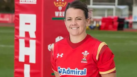 Sian Williams A photo of Sian Williams in Wales rugby gear, standing to attention by a padded goalpost on the field
