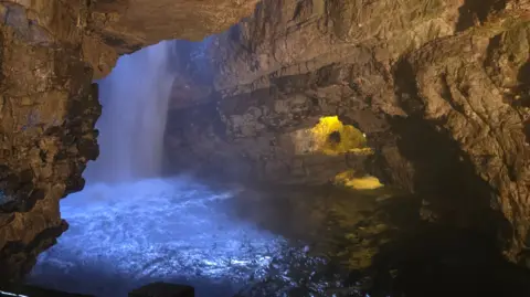Steffi Franke A waterfall inside a cave, with part of the cave lit by yellow light