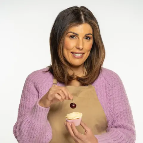 Channel 4 Georgie smiles holding a cupcake