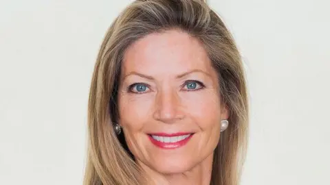 Jennifer Houghton Jennifer, una mujer de sonrisa brillante, tiene cabello largo castaño claro.