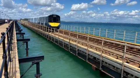 A picture of a train riding along a line fixed above the sea on the Island Line 