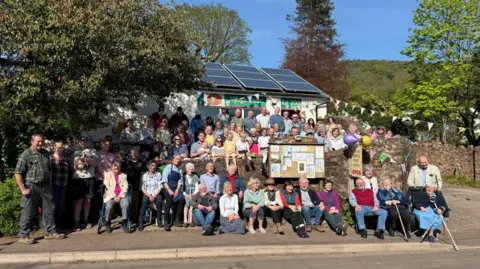 A group of people is standing outside a shop in the sun. 